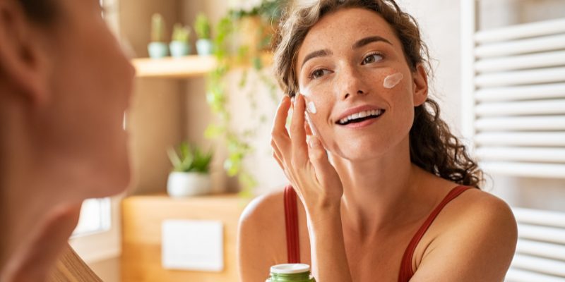 Woman putting on moisturizer in a mirror